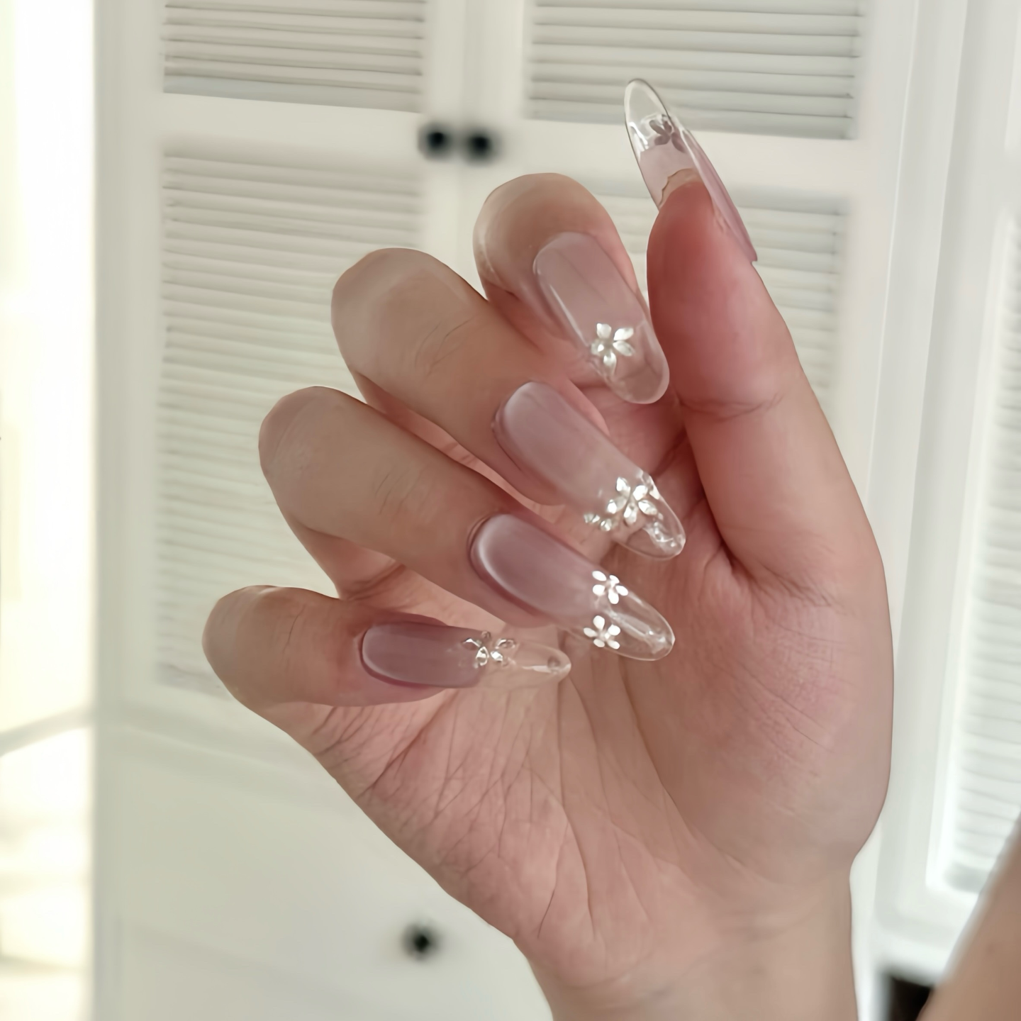 Hand with clear acrylic nails featuring floral designs against a neutral background