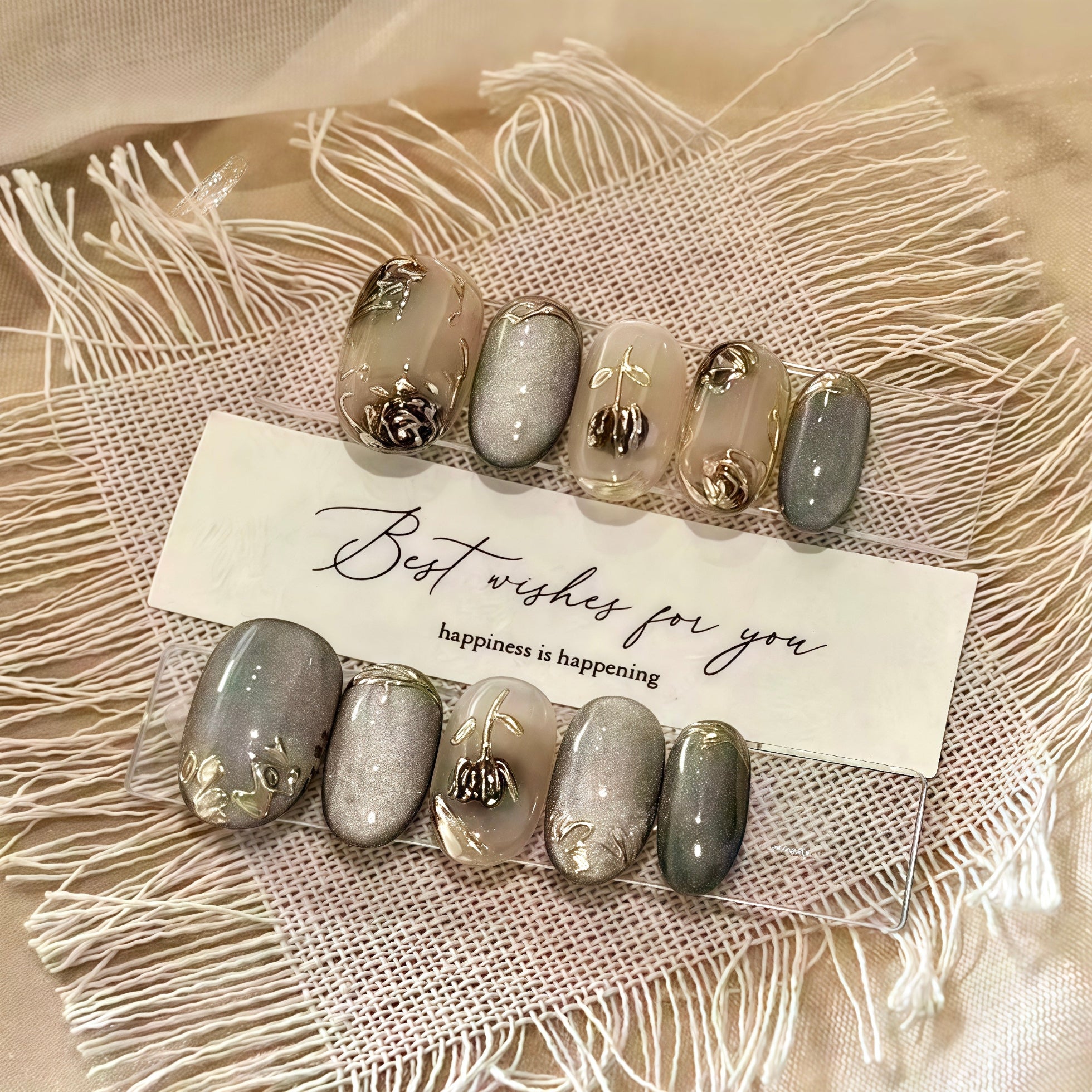 Set of decorative nails with gold accents on a textured surface with a card reading 'Best wishes for you, happiness is happening'.