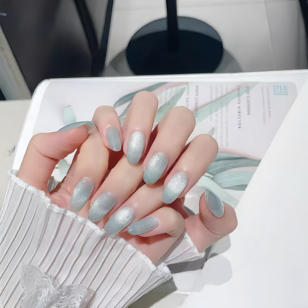 Hand with light blue glittery nail polish on a blurred background