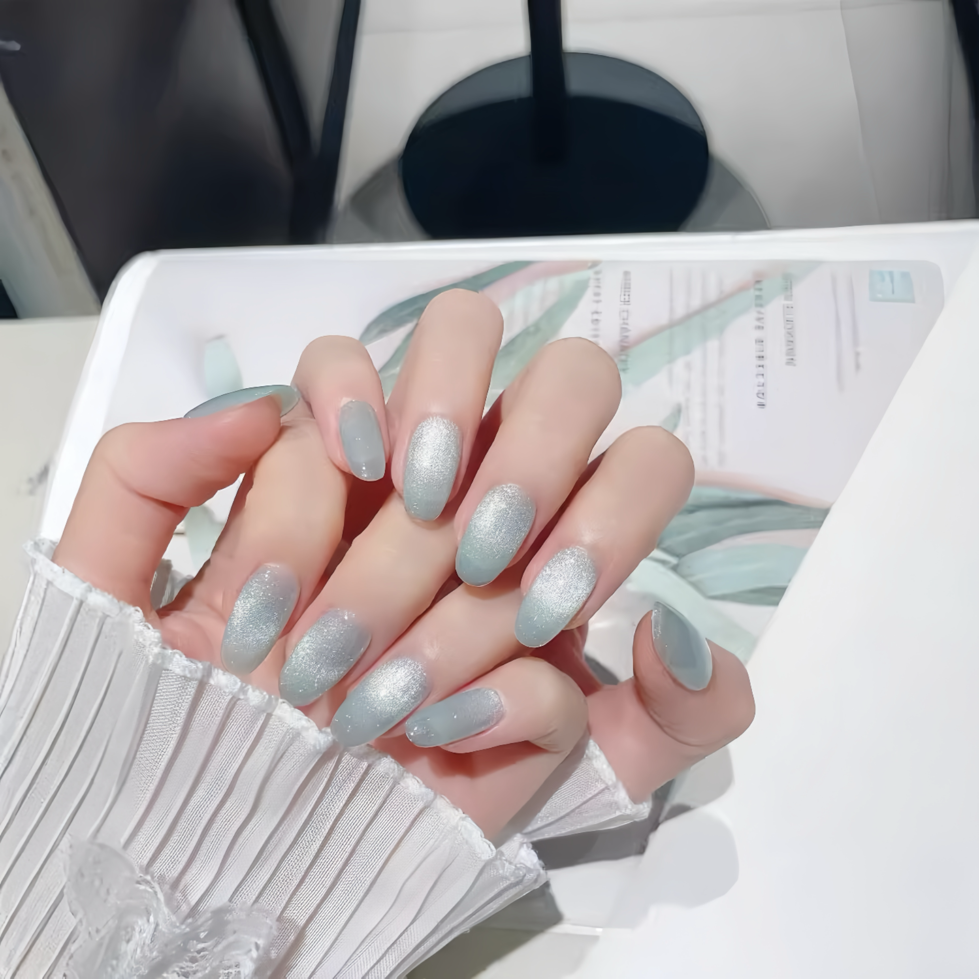 Hand with light blue glittery nail polish on a blurred background