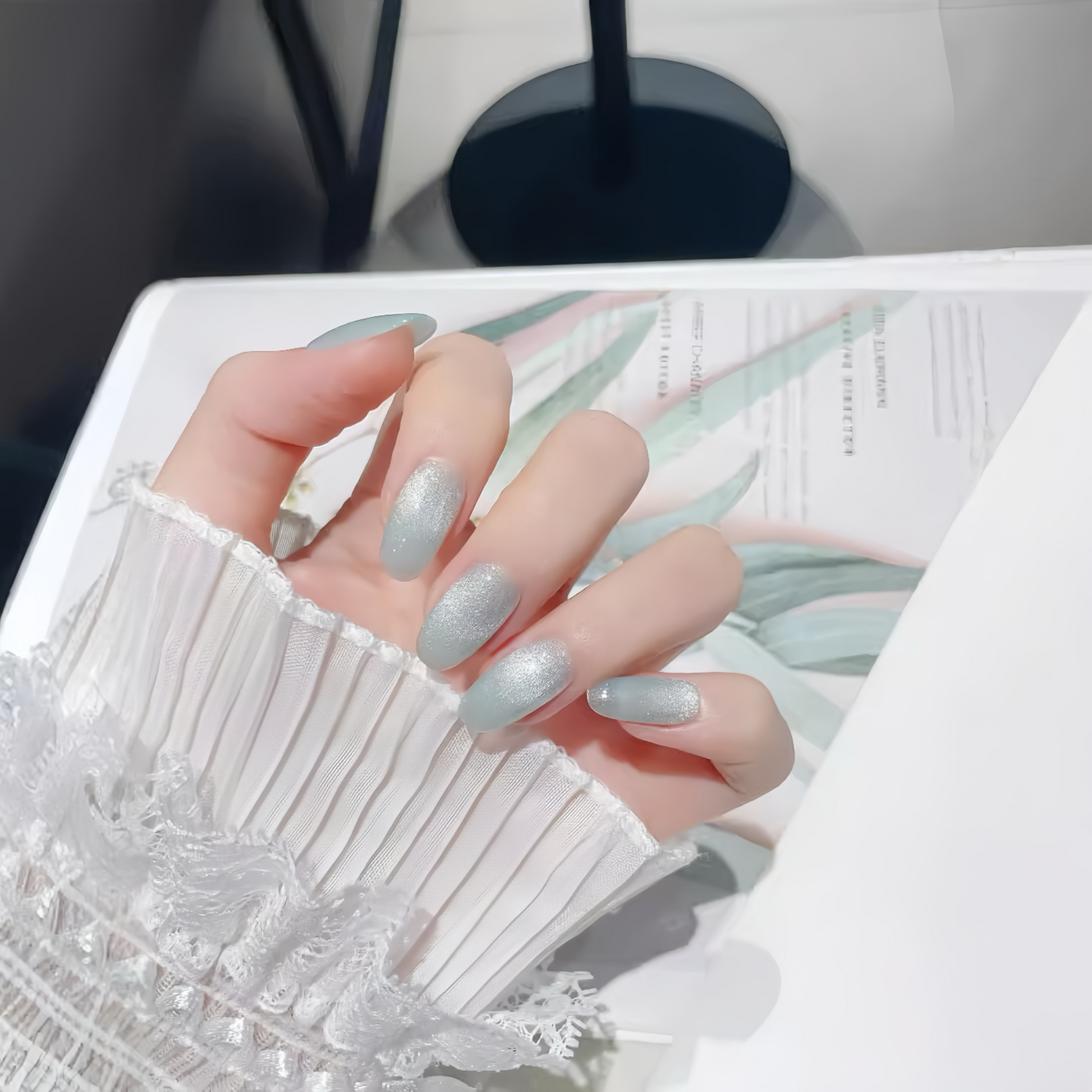 Hand with light gray nail polish on a white surface with floral design
