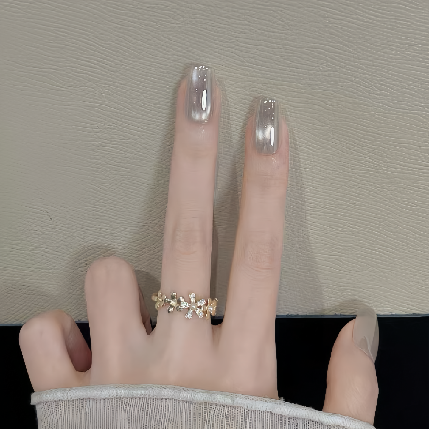 Hand wearing a decorative ring with clear nail polish on a neutral background