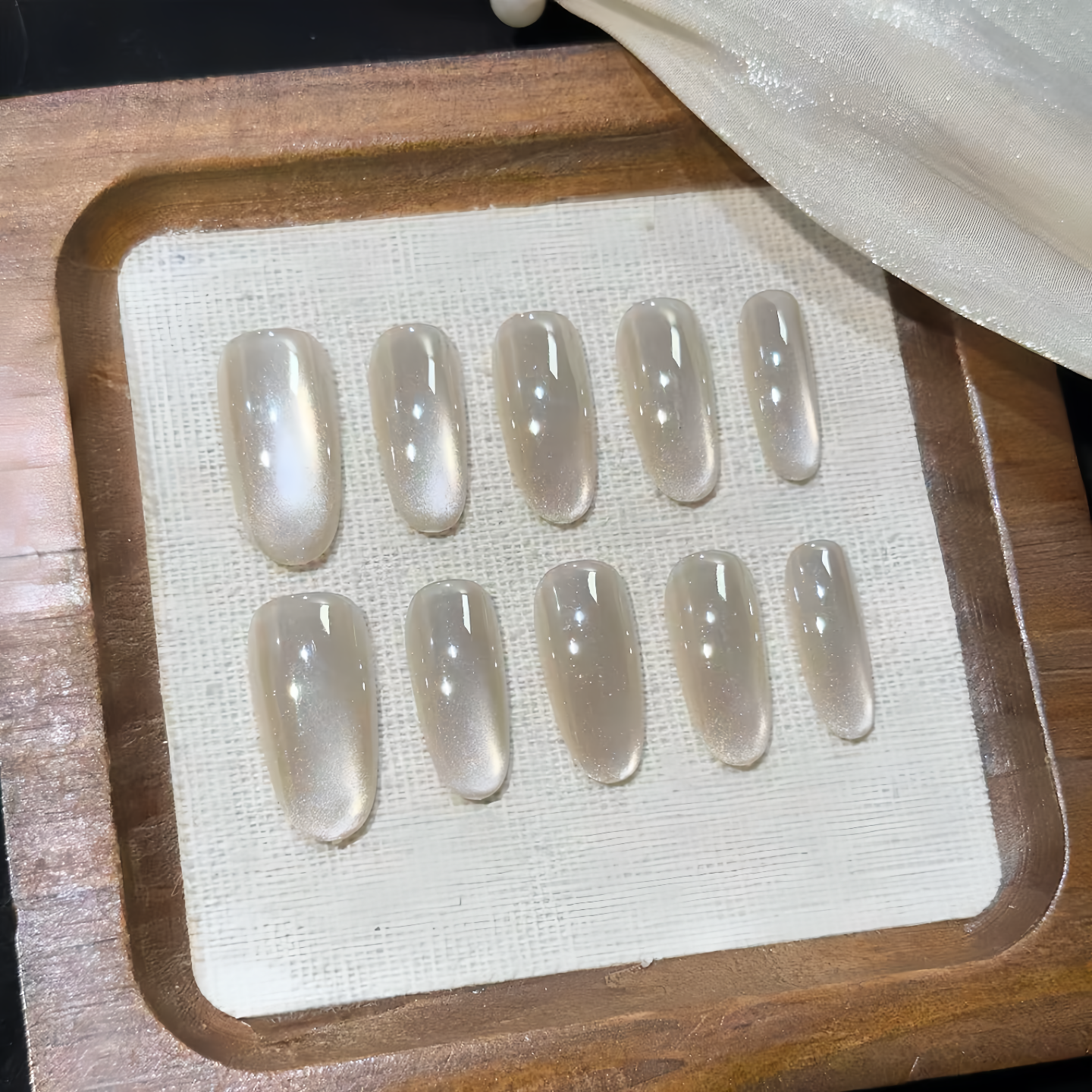 Set of clear nail extensions on a wooden tray with a white cloth