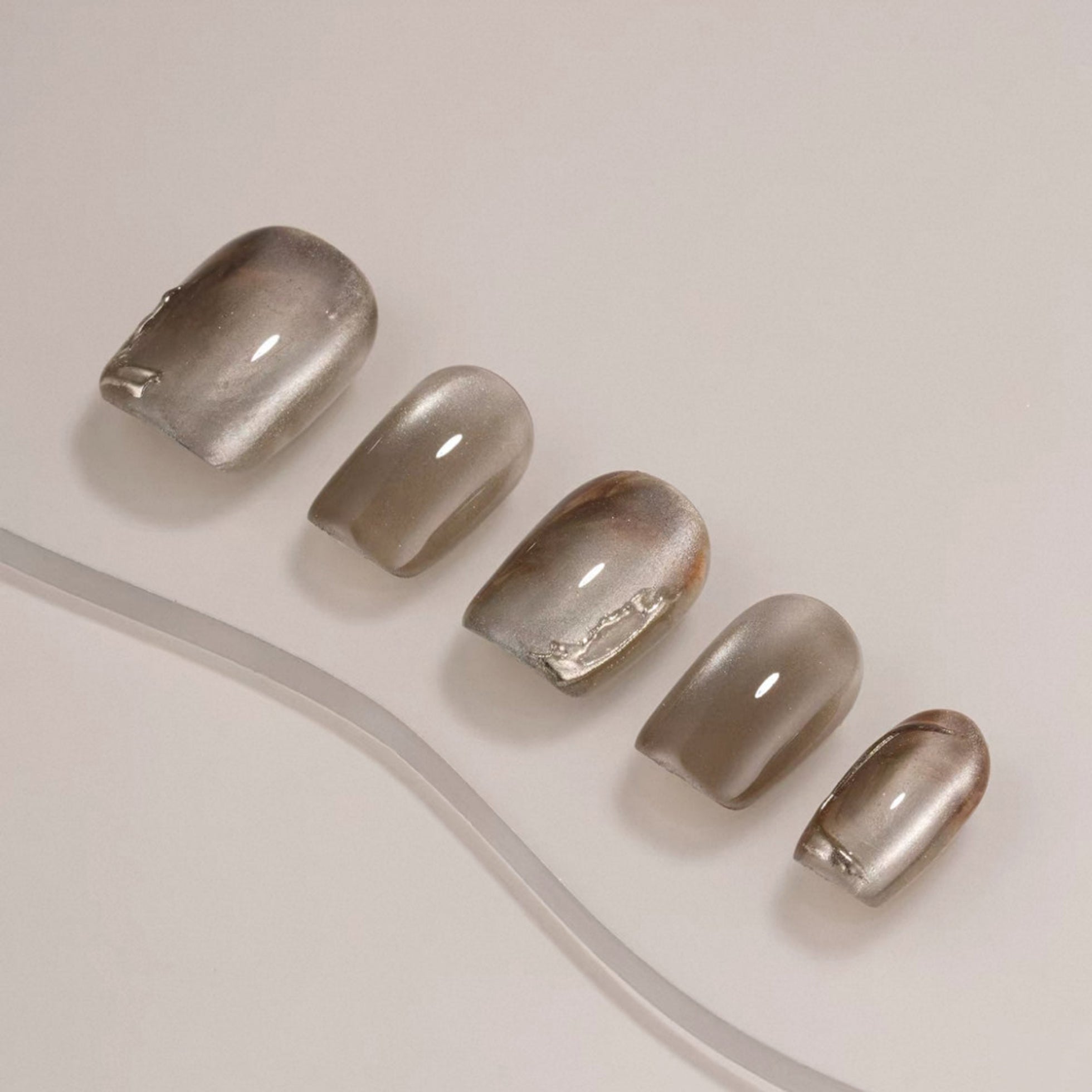 Set of five metallic gray nail polish samples on a light background