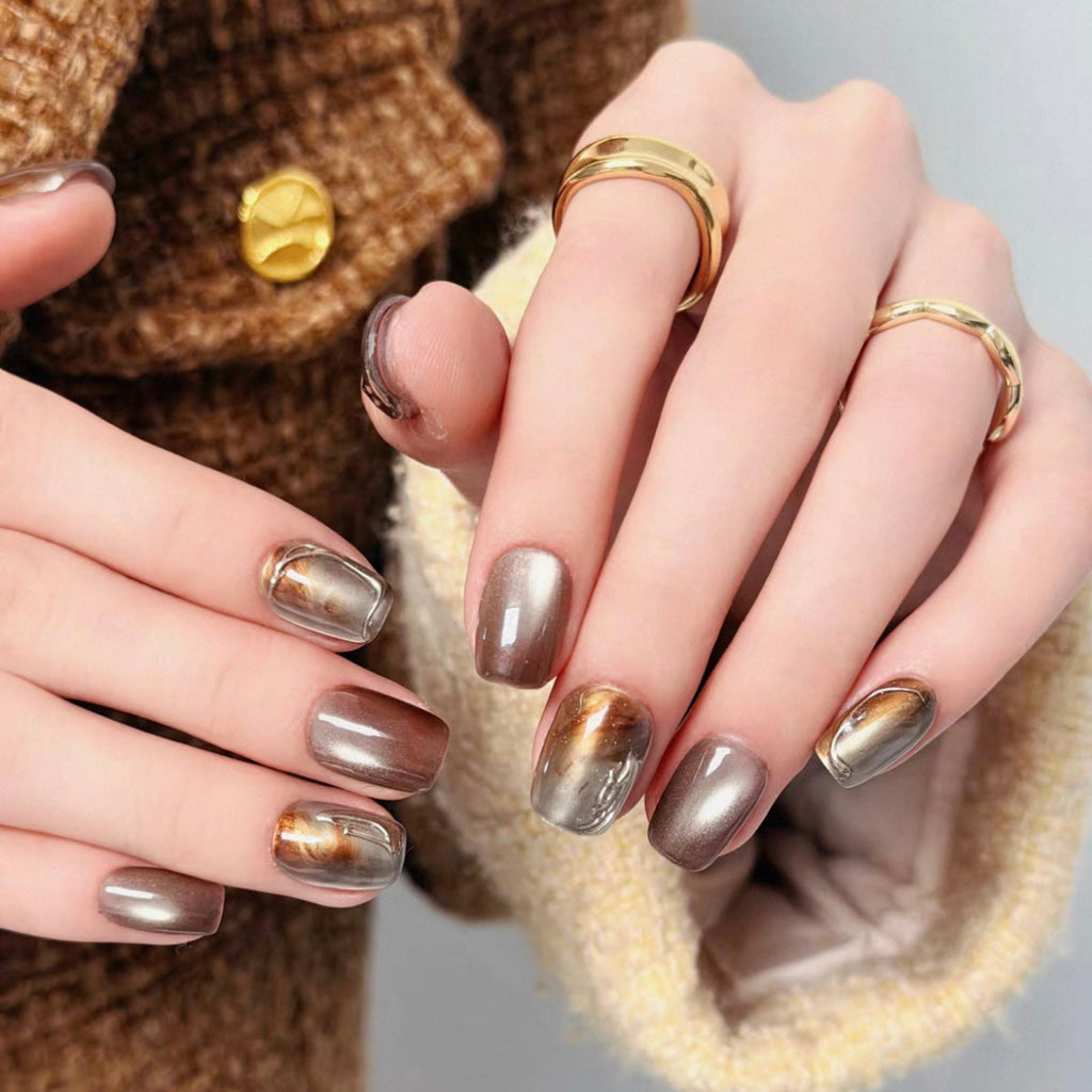 Close-up of hands with metallic nail polish wearing gold rings, against a neutral background.