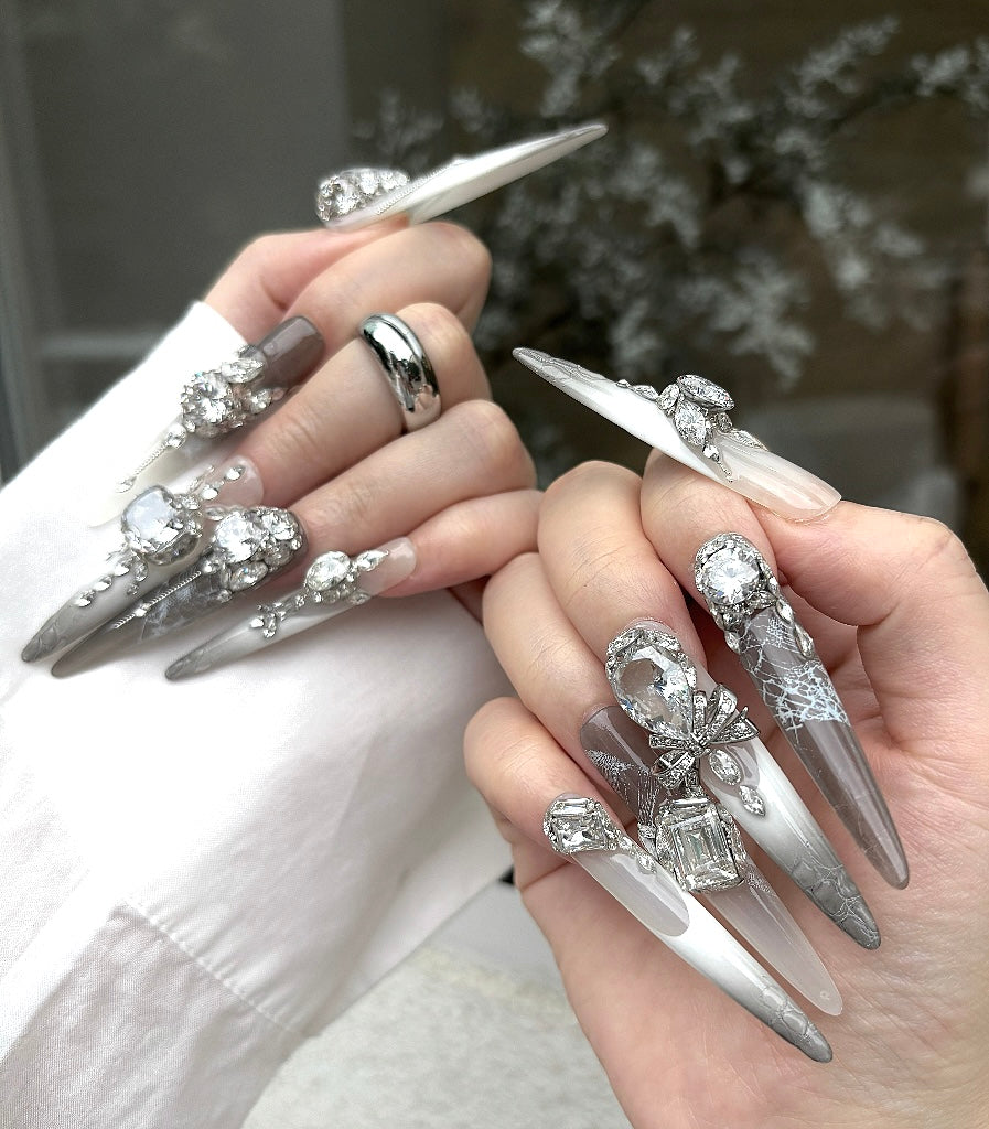 Close-up of hands with long, pointed nails featuring diamond-like gemstones.
