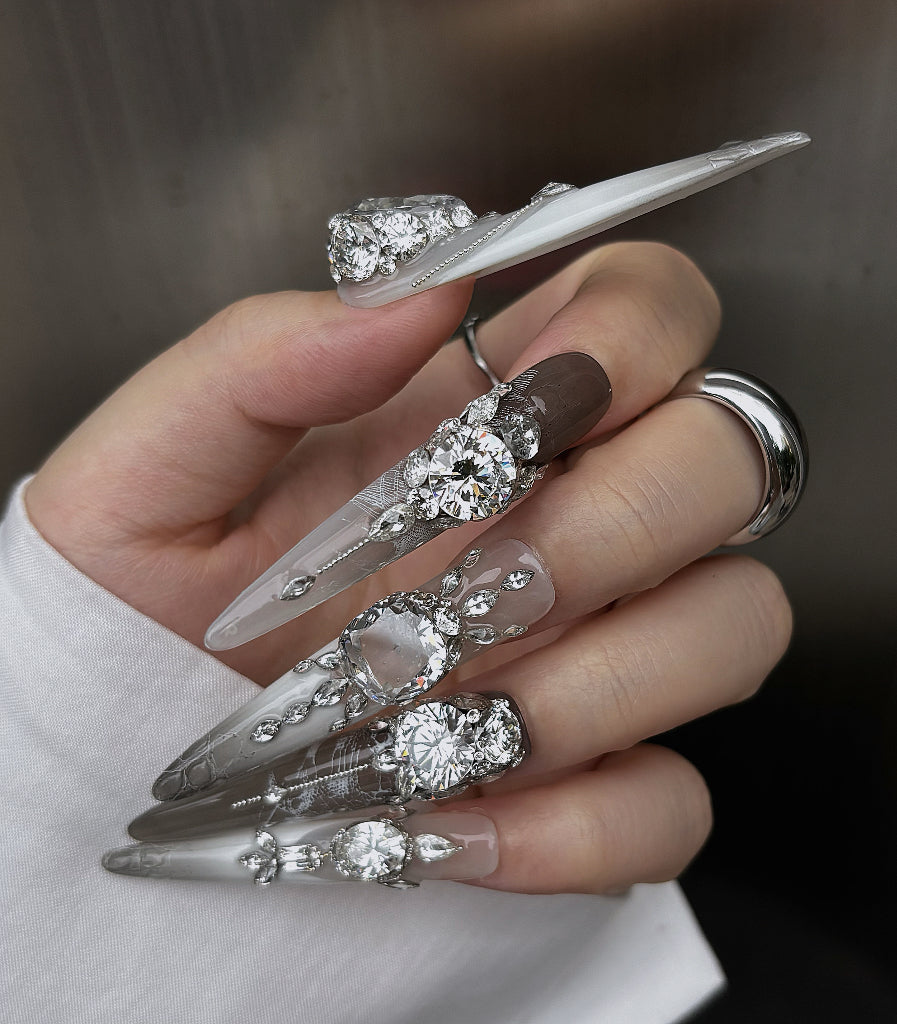 Hand with decorative nail art featuring crystals and clear polish on a neutral background