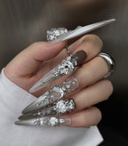 Hand with decorative nail art featuring crystals and clear polish on a neutral background