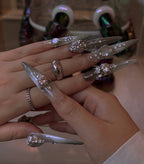 Close-up of a hand with long, decorative nails and rings.