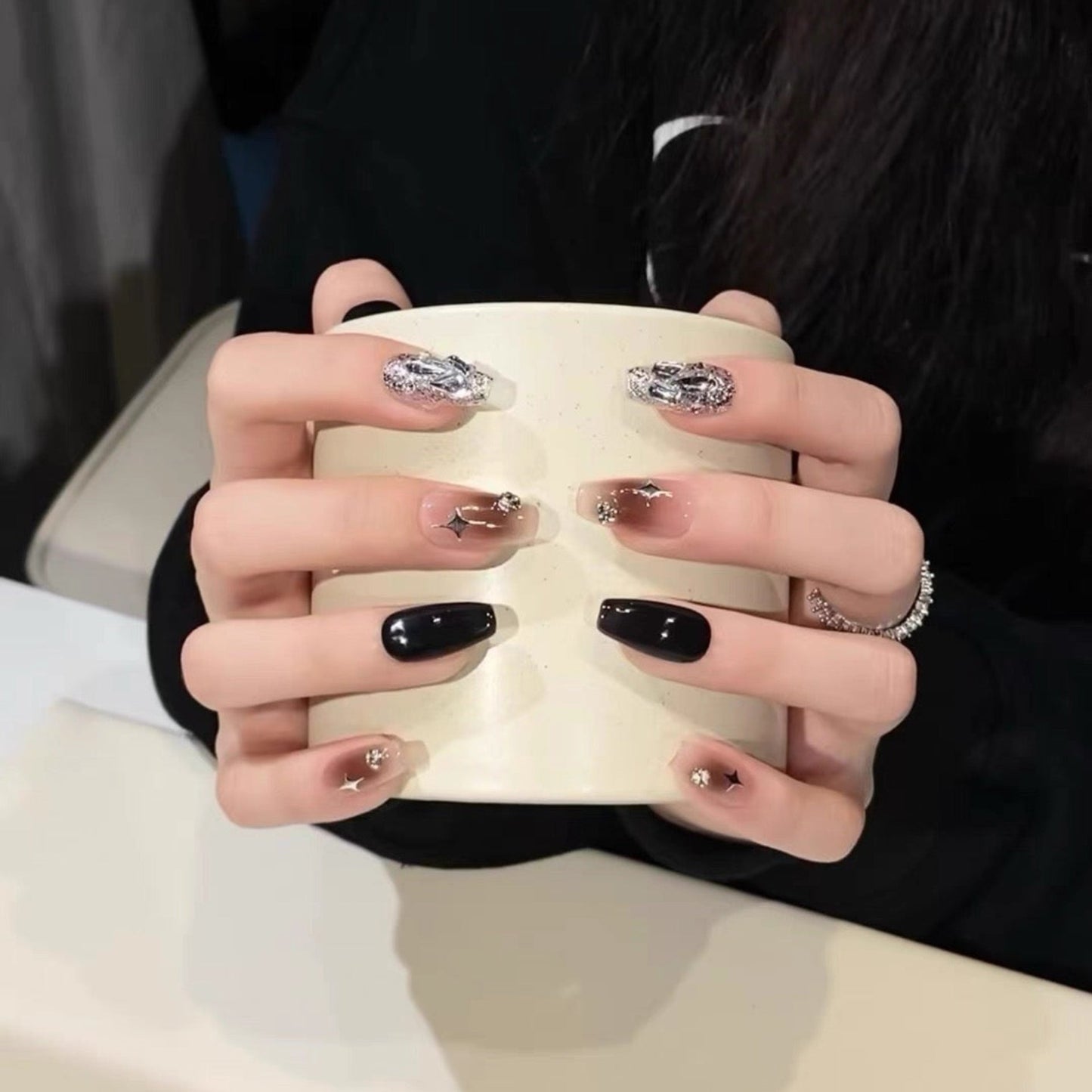Close-up of a hand with black and gold nail design holding a white mug.