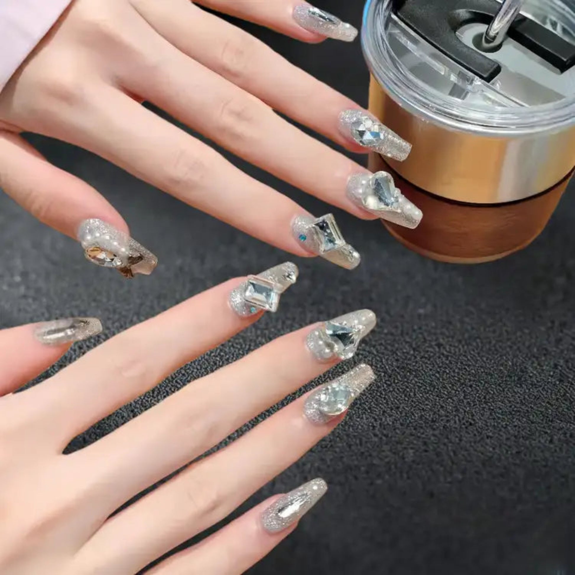 Hand with decorative nails holding a metallic cup on a textured surface