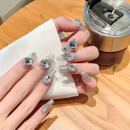 Hand with diamond-shaped nail art holding a metallic cup on a wooden surface