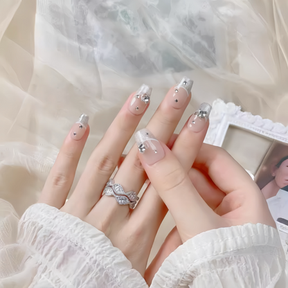 Close-up of hands with decorative nails and a ring, wearing a white textured garment.