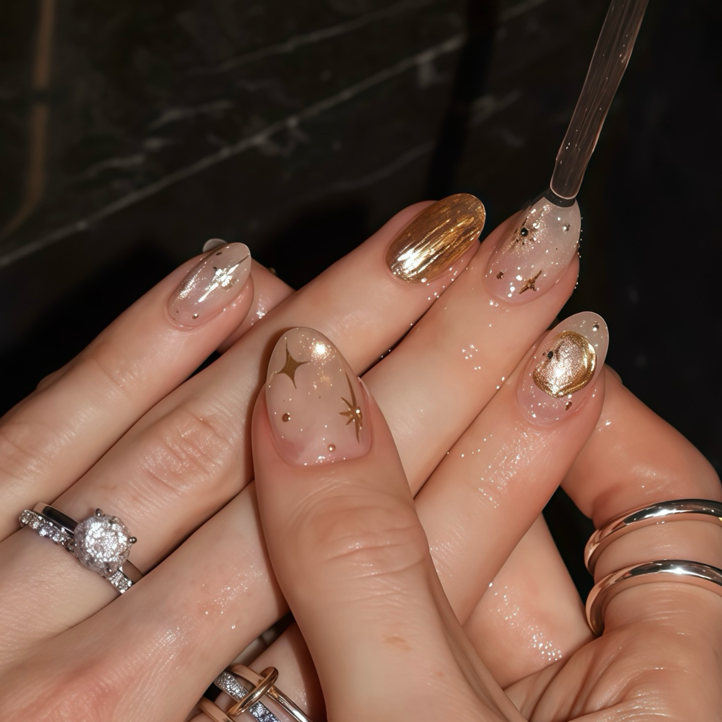 Close-up of hands with gold and clear nail polish on a dark background