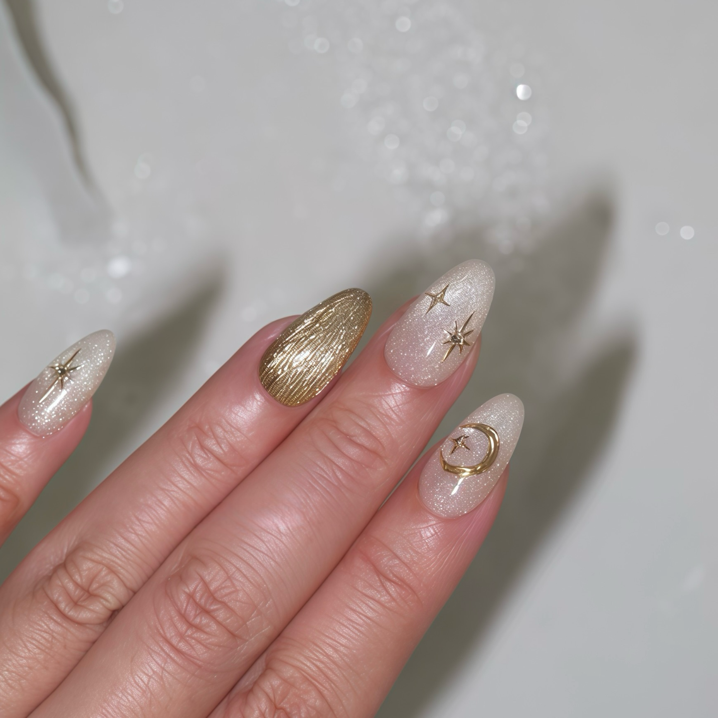 Hand with decorative nails featuring gold and star designs on a neutral background
