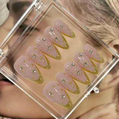 Set of decorative false nails with pink and gold design in a clear case.