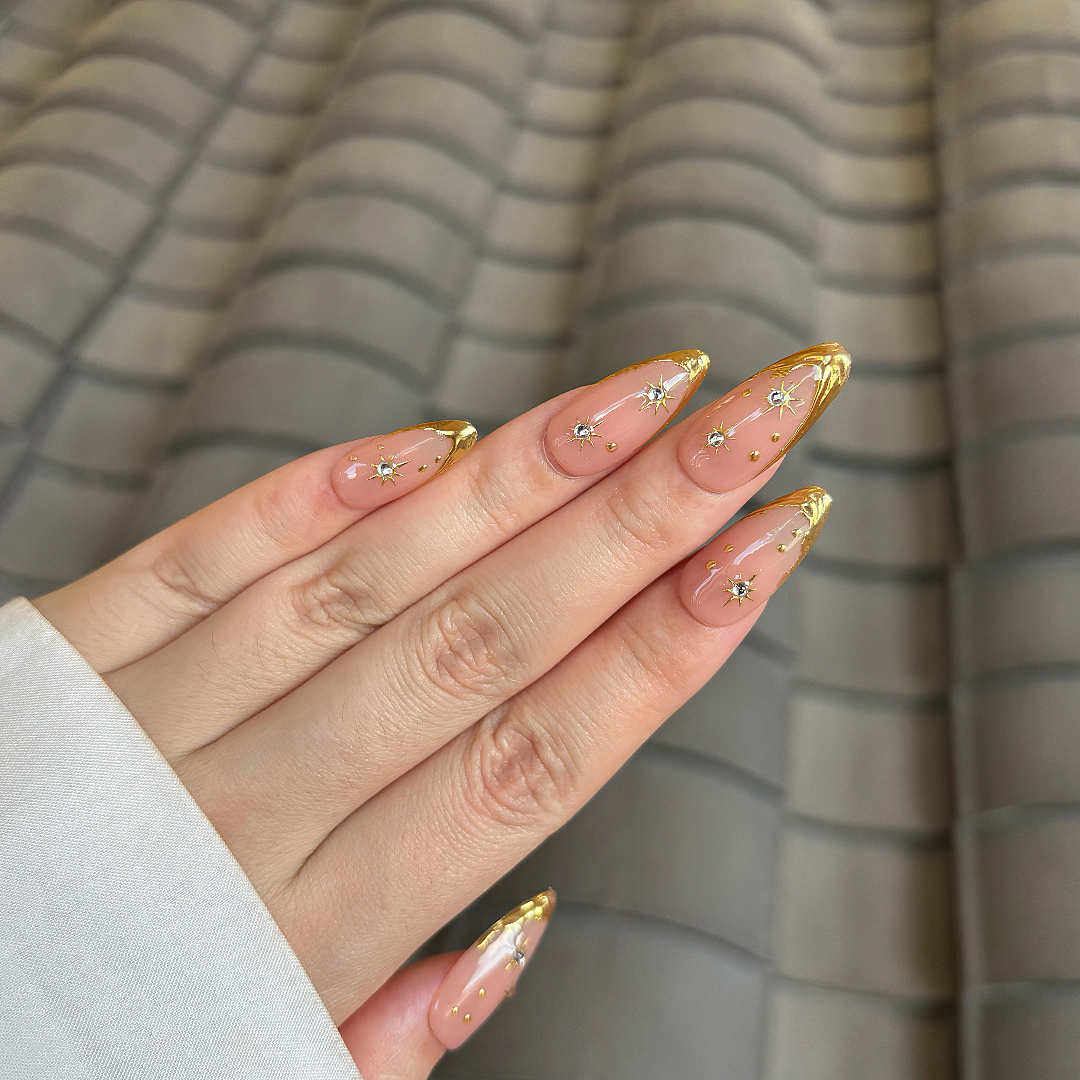 Hand with gold and clear nail polish against a striped background