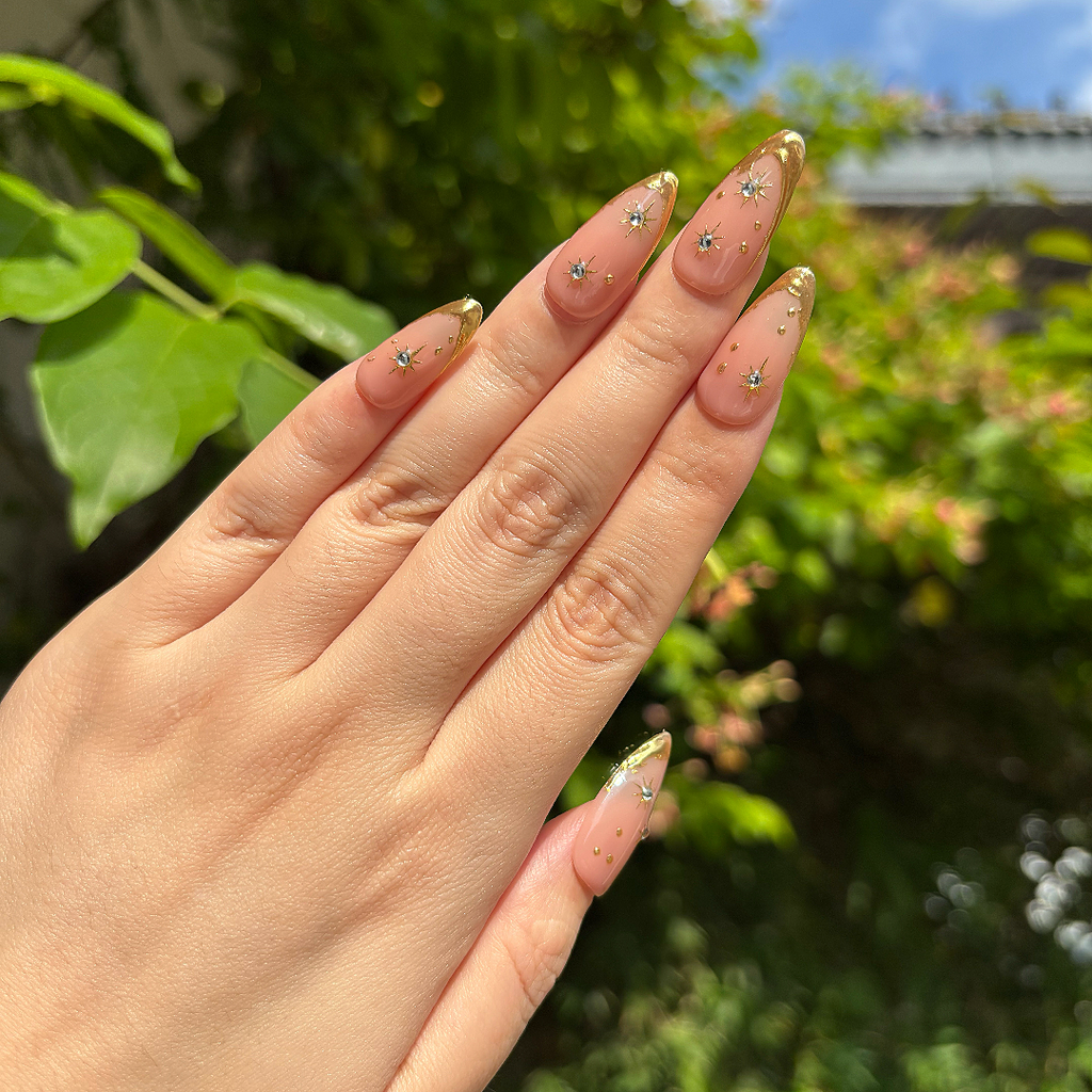 Hand with decorative nails against a blurred green outdoor background