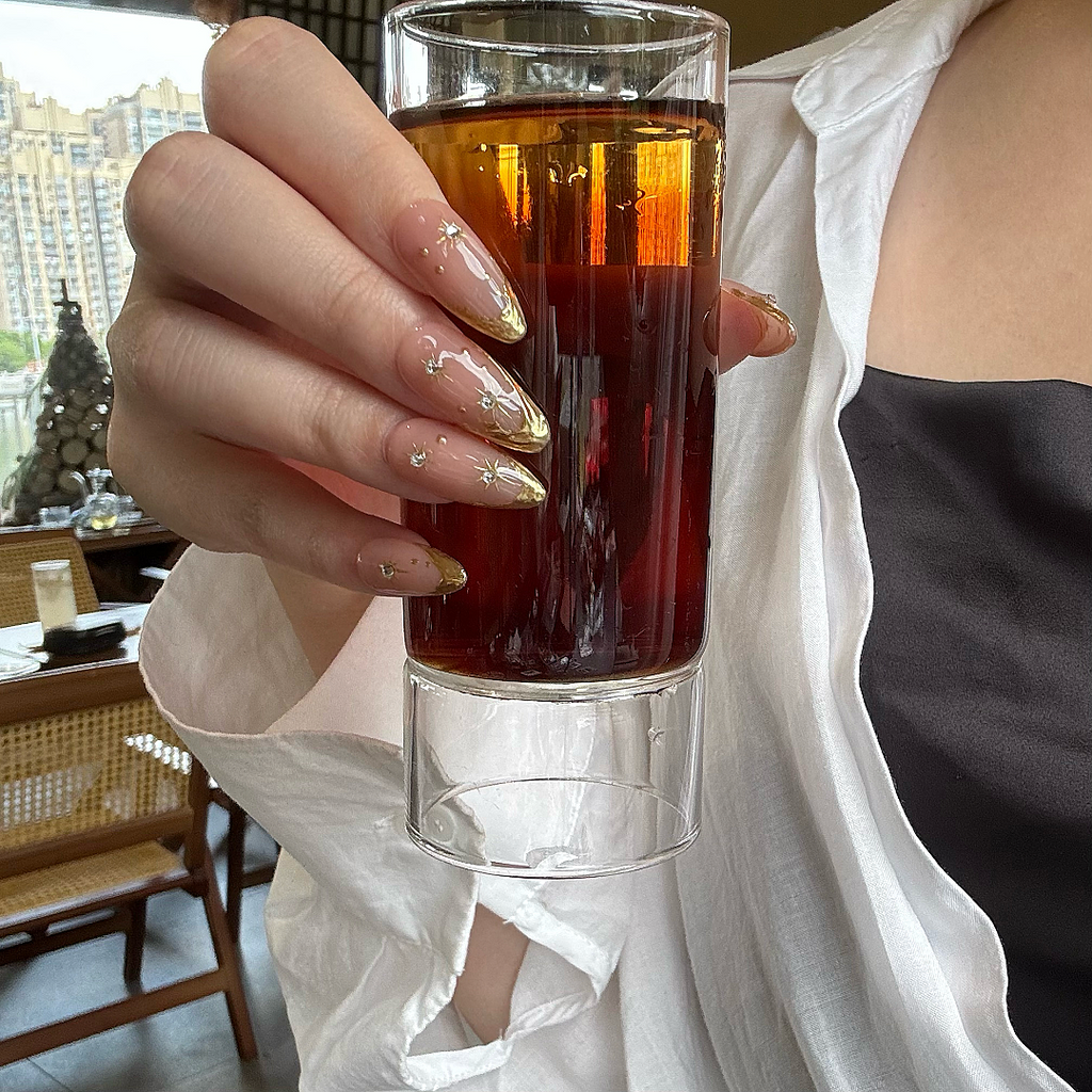 Hand holding a glass of amber liquid with a blurred indoor background