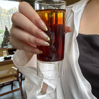 Hand holding a glass of amber liquid with a blurred indoor background