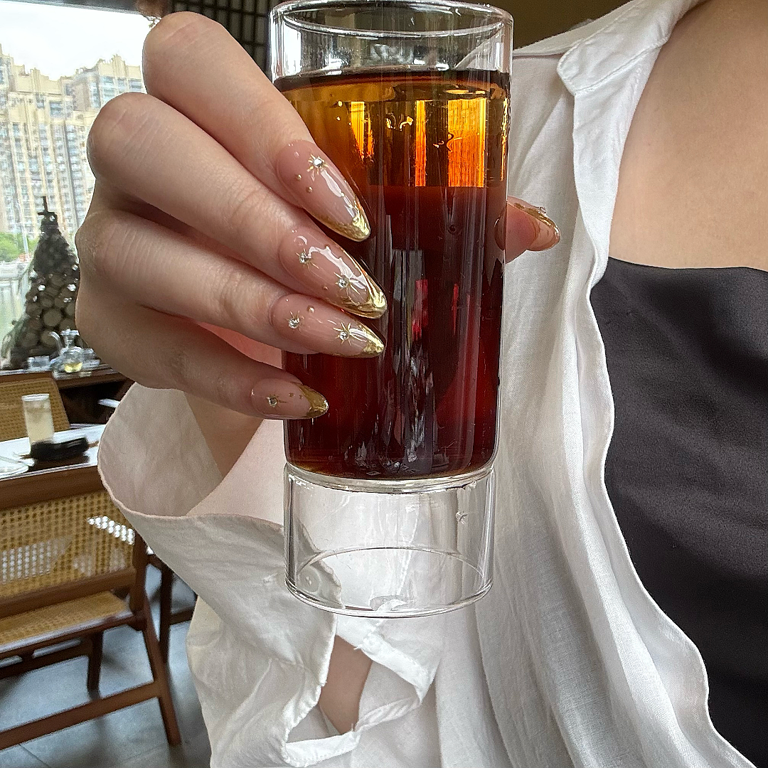 Hand holding a glass of amber liquid with a blurred indoor background
