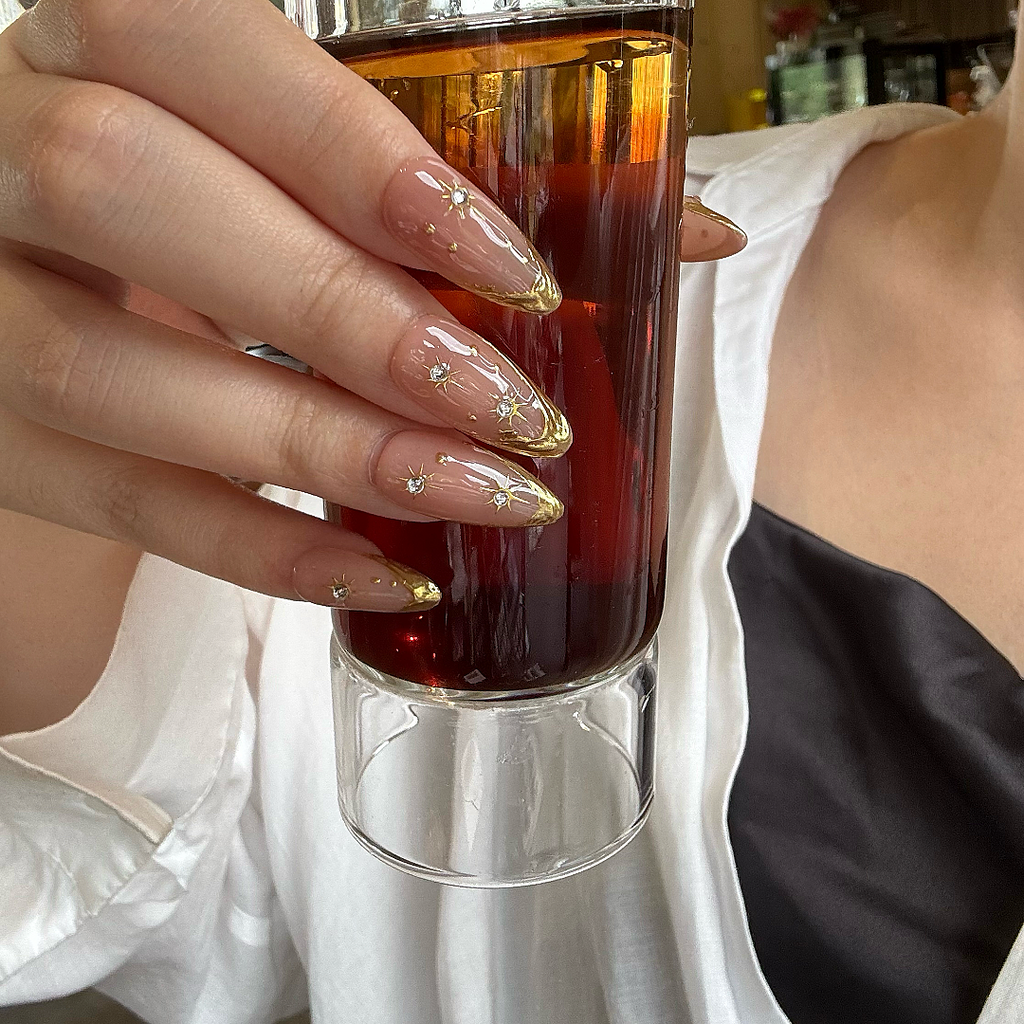 Hand with decorative nails holding a glass of red wine.