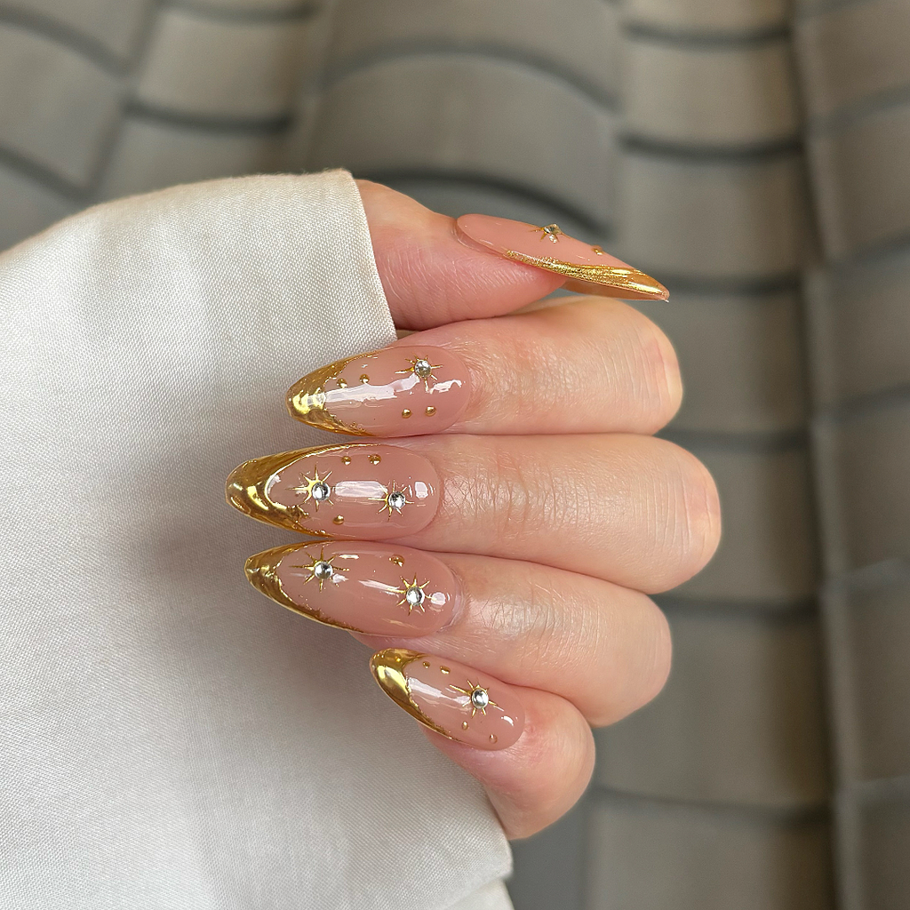 Hand with gold-accented nails holding a white object against a neutral background