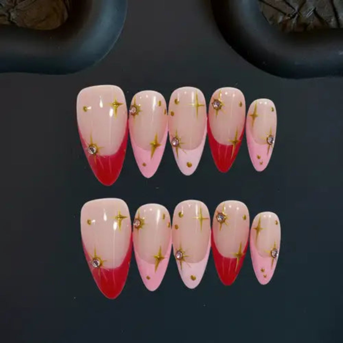 Set of nail art designs with red and pink gradient and gold star decorations on a dark background.