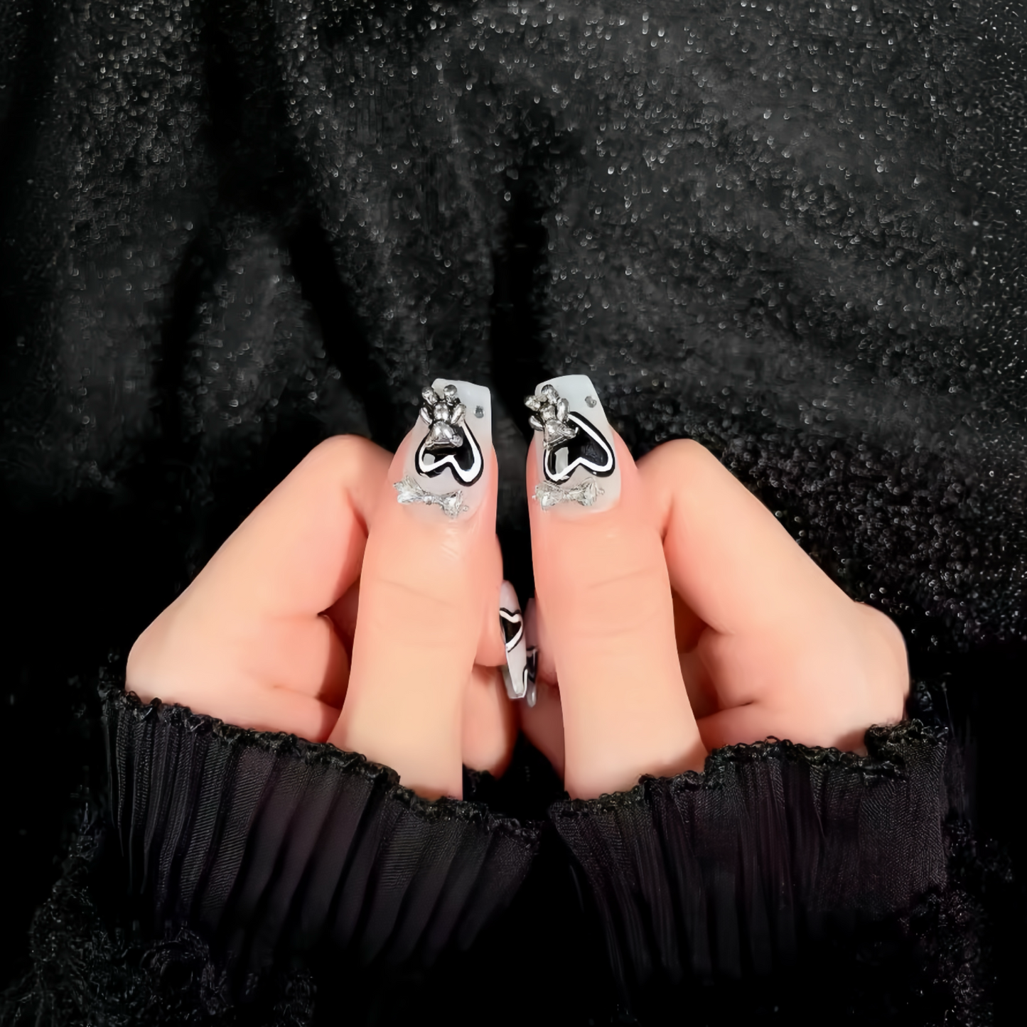 Silver earrings with black heart designs held between fingers against a black textured background