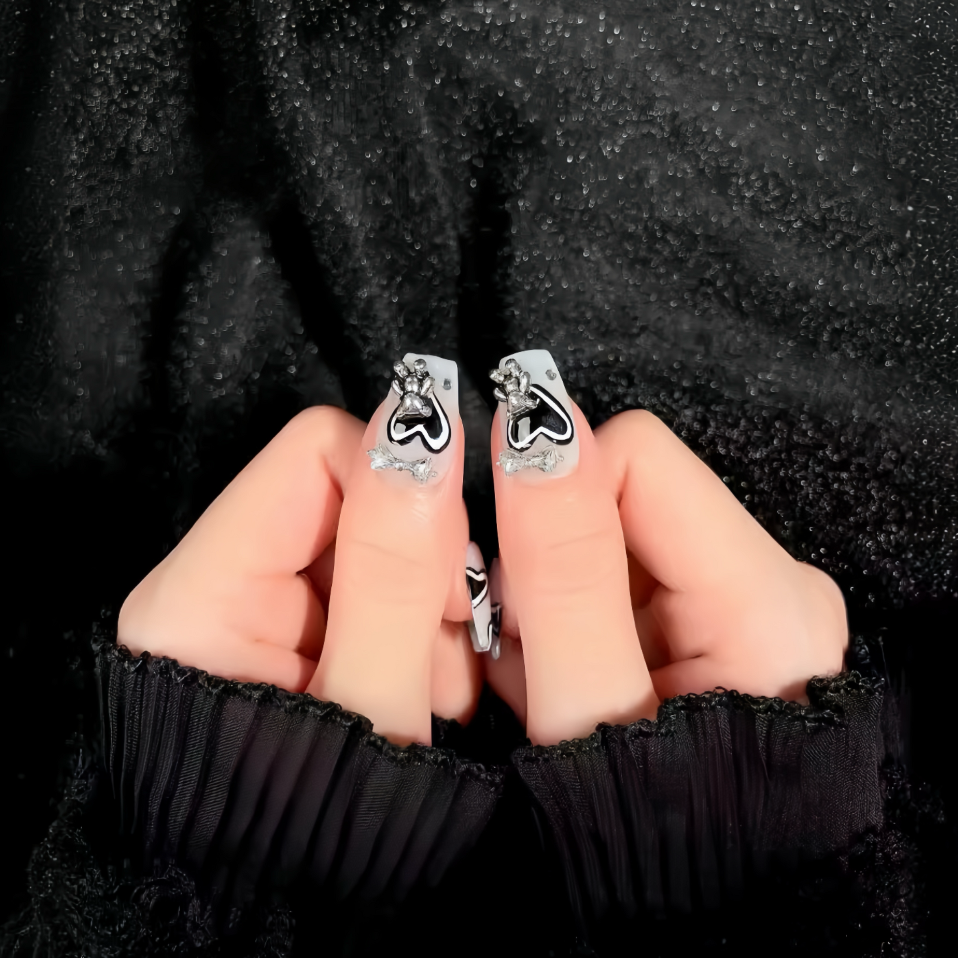 Silver earrings with black heart designs held between fingers against a black textured background