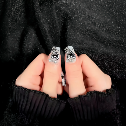 Silver earrings with black heart designs held between fingers against a black textured background
