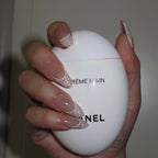 Hand holding a Chanel hand cream against a plain background