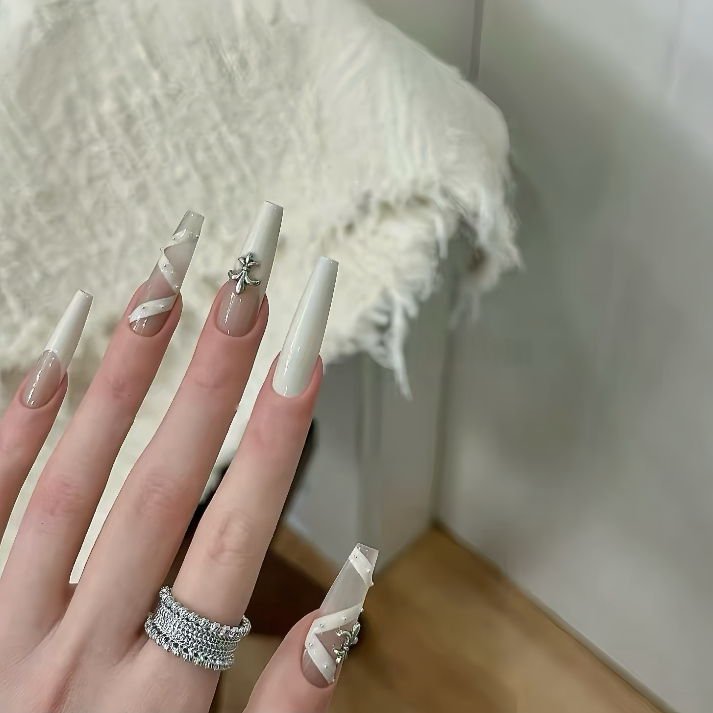 Hand with white nail polish and silver rings against a neutral background