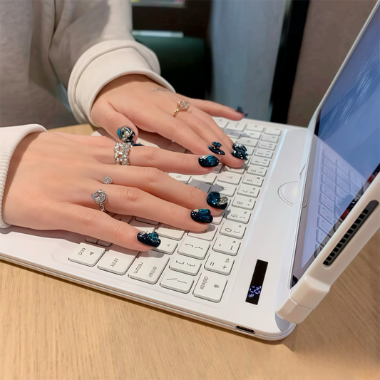 Person typing on a laptop with decorative nail art and rings.