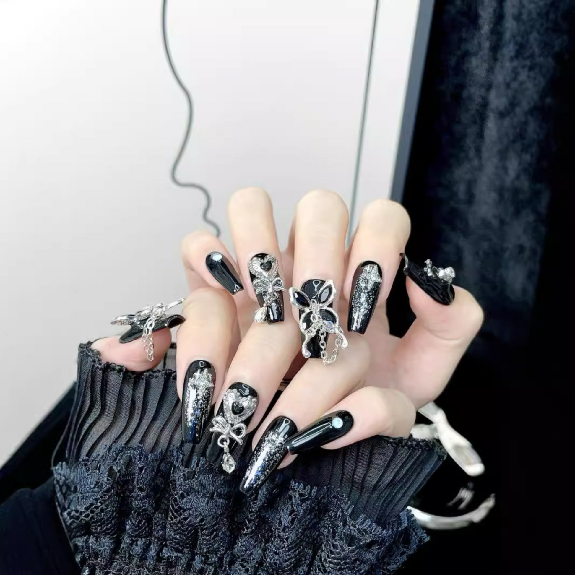 Close-up of a hand with black nail art featuring silver decorations against a neutral background.