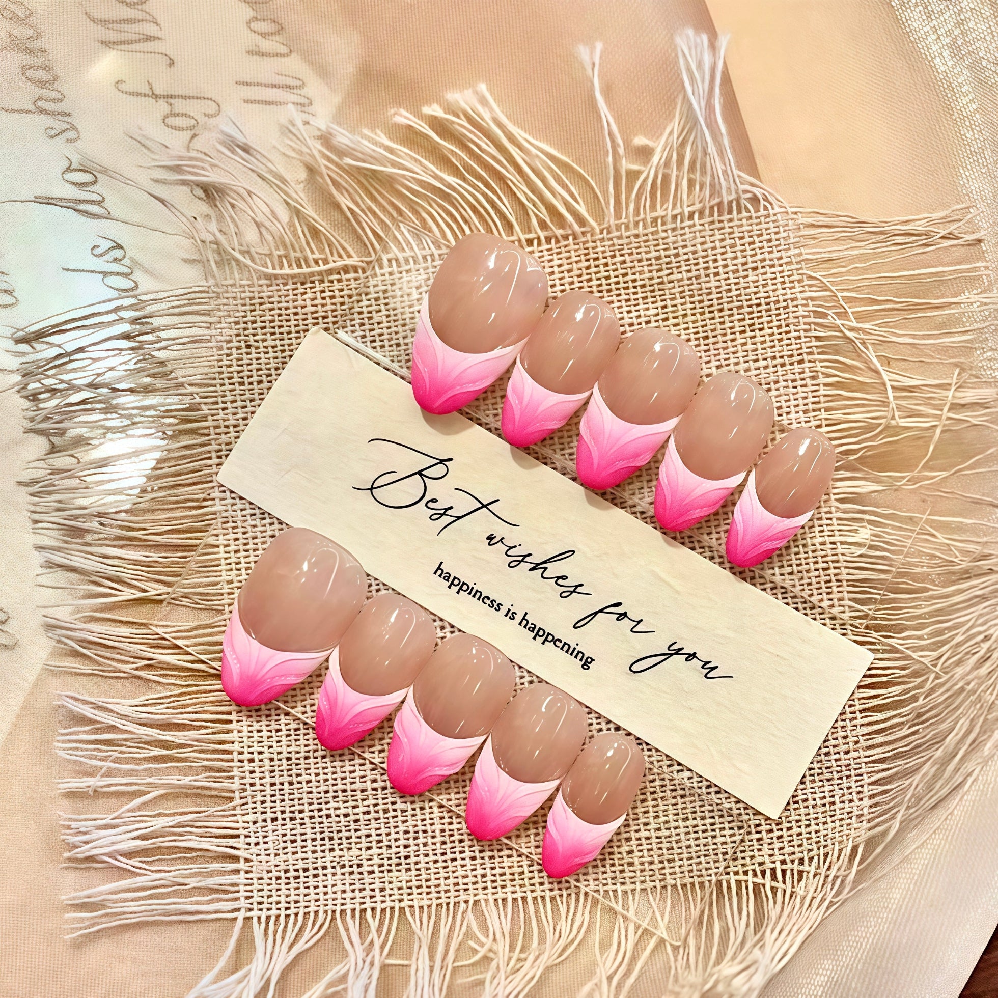 Set of pink and brown gradient nails on a textured surface with a card reading 'Best wishes for you happiness is happening'.